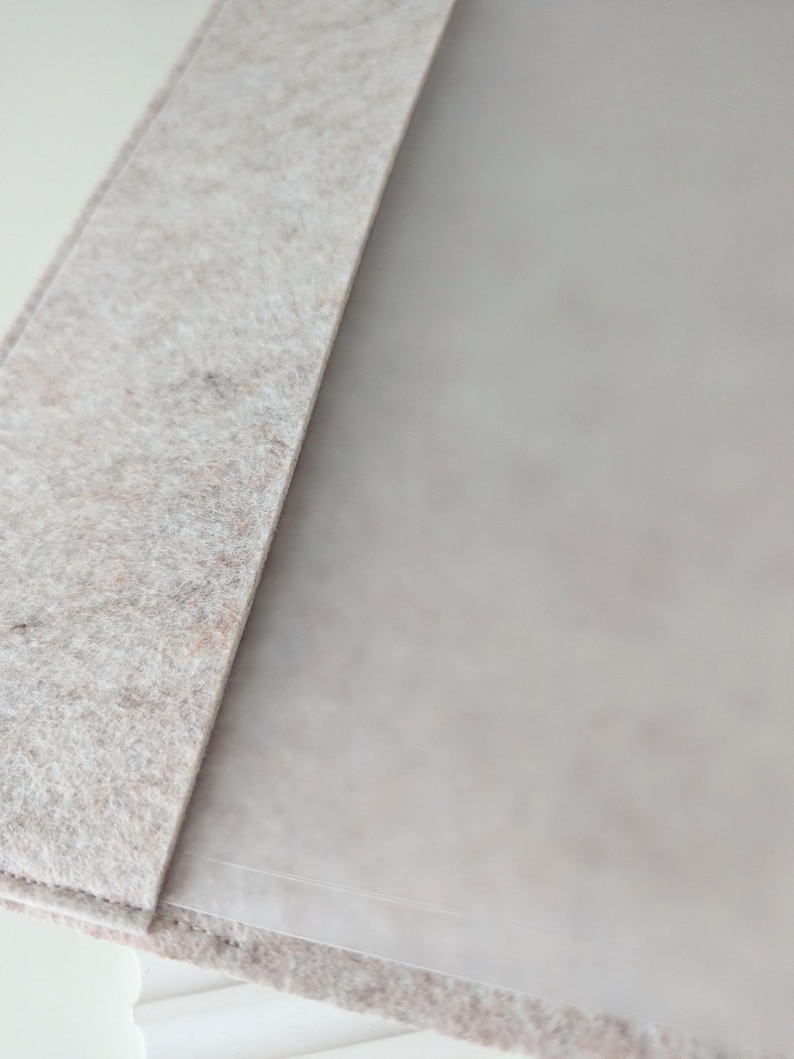 May include: A light beige felt folder featuring a textured, fibrous surface with a soft, matte appearance. The folder has a clean, straight edge and a smooth, semi-transparent interior panel that is partially visible, showing a subtle, neutral tone.