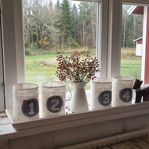 May include: A set of four off-white fabric pouches, each featuring a circular blue patch with a white number from one to four. The pouches are arranged on a white windowsill next to a white pitcher containing red berries and a small wooden deer figure.