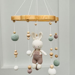 Pode incluir: Um móbile de bebé de madeira com um coelho de crochet, bolas verdes e castanhas e contas de madeira.