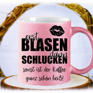 Könnte beinhalten: Rosa Glitzer-Kaffeetasse mit schwarzem Text "erst blasen dann schlucken sonst ist der kaffee ganz schön heiß!" und einem schwarzen Lippenabdruck.