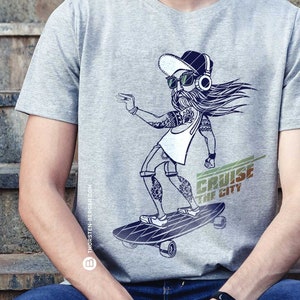 Könnte beinhalten: Ein graues T-Shirt mit einem Grafikdruck eines Comic-Charakters, der Skateboard fährt. Der Charakter trägt eine Mütze, Sonnenbrille und Kopfhörer. Der Text "CRUISE THE CITY" ist auf dem Shirt aufgedruckt.
