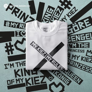 Könnte beinhalten: Weißes T-Shirt mit einem schwarzen X-Design und dem Text "MY KIEZ MY RULES" darauf gedruckt. Das T-Shirt ist gefaltet und auf einem blauen Hintergrund mit schwarzem Text abgebildet.