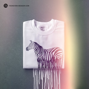 May include: White t-shirt with a black and white zebra graphic. The zebra is dripping with black paint, creating a unique and artistic design.