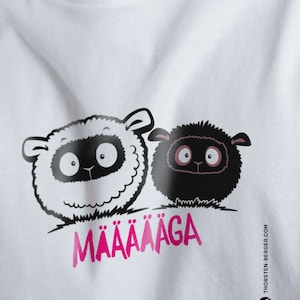 May include: White t-shirt featuring a black and white illustration of two sheep with large eyes. The text "MÄÄÄÄÄGA" is printed in pink below the sheep.