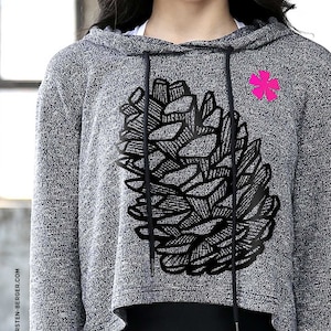 May include: A gray and white cropped hoodie with a black pine cone design and a pink flower graphic. The hoodie has a drawstring hood.