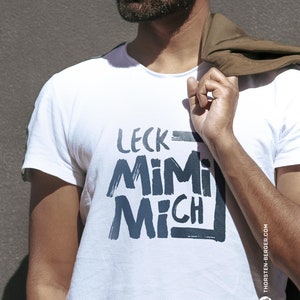 May include: White t-shirt with a black and white graphic print that says "LECK MIMI MICH" and a small black and white logo in the bottom right corner that says "THORSTEN-BERGER.COM".