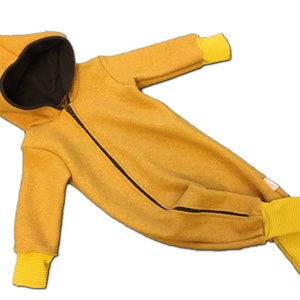 Peut inclure: Une grenouillère jaune pour bébé avec une fermeture éclair noire et des poignets jaunes. La grenouillère a une capuche avec une doublure noire.