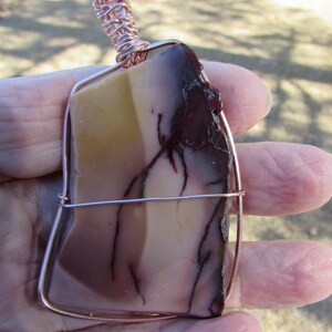 Puede incluir: Un colgante envuelto en alambre de cobre con una piedra natural con patrones marrones, rojos y amarillos.