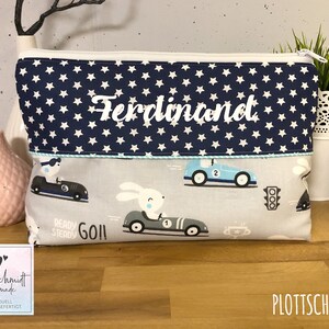 Puede incluir: Una bolsa de aseo azul y blanca con un patr&oacute;n de estrellas blancas y el nombre "Ferdinand" bordado en la parte delantera. La bolsa tiene un dise&ntilde;o de coche azul y blanco en la parte inferior con las palabras "Ready Steady Go!" impresas en ella.