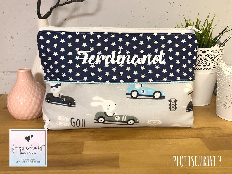 Puede incluir: Una bolsa de aseo azul y blanca con un patr&oacute;n de estrellas blancas y el nombre "Ferdinand" bordado en la parte delantera. La bolsa tiene un dise&ntilde;o de coche azul y blanco en la parte inferior con las palabras "Ready Steady Go!" impresas en ella.