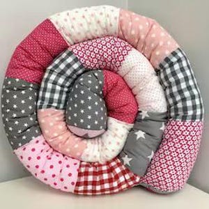 Op de afbeelding: Een roze en grijze patchwork baby speelmat in de vorm van een spiraal. De mat is gemaakt van verschillende stoffen met verschillende patronen, waaronder stippen, sterren en bloemen.