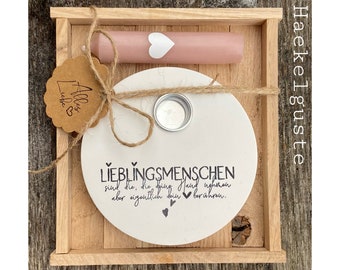 Peut inclure: Un plateau en bois contient une bougie rose avec un cœur blanc, un dessous de verre circulaire blanc avec du texte allemand et une petite étiquette. Le dessous de verre a un bougeoir en métal et est attaché avec de la ficelle. L'étiquette dit "Alles Liebe".