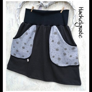 Könnte beinhalten: Ein schwarzer und grauer Rock mit hohem Bund. Der Rock hat ein schwarz-weißes Tupfenmuster und graue Taschen mit einem Pusteblumen-Design. Der Text "Haeckelguste" ist auf der rechten Seite des Bildes zu sehen.