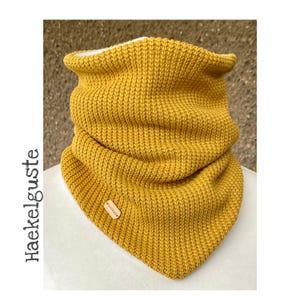 Könnte beinhalten: Ein senfgelber gestrickter Halsschmuck mit dreieckiger Form und einem kleinen Holzetikett.