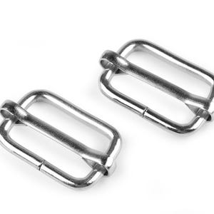 Könnte beinhalten: Zwei silberne Metall-Schieber-Schnallen für Riemen oder Gürtel.