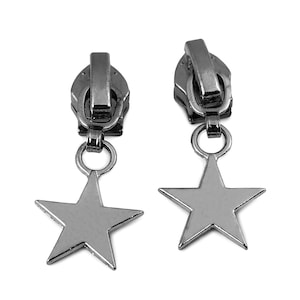 Könnte beinhalten: Zwei Reißverschlussanhänger in Gunmetal-Farbe mit sternförmigen Anhängern. Die Reißverschlussanhänger sind dunkelgrau-metallisch, und die Sternanhänger sind mit einem kleinen Ring befestigt. Der Hintergrund ist weiß.