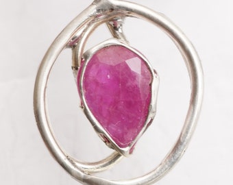 May include: A silver pendant featuring a pink gemstone set within a circular frame. The pendant hangs from a silver chain.