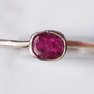 Op de afbeelding: Een zilveren ring met een roze edelsteen in een bezel-setting.