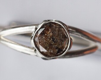 May include: A silver ring with a brown, faceted gemstone set in a bezel setting.