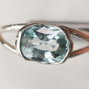 May include: A silver ring with a light blue oval gemstone set in a textured band.