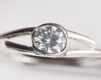 May include: A silver ring with a single, clear, round gemstone set in a bezel setting.