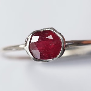 Pode incluir: Um anel de prata com uma gema de rubi vermelho engastada em uma banda texturizada.