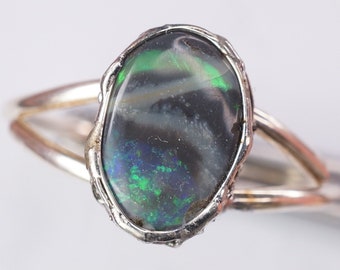 May include: A silver ring with an oval-shaped black opal gemstone. The opal has green and blue flashes of color.