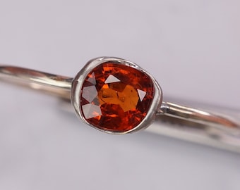 Könnte beinhalten: Ein silberner Ring mit einer Zargenfassung, in der ein quadratischer orangefarbener Edelstein sitzt.