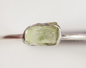 May include: A silver ring with a raw, light green gemstone set in the center.
