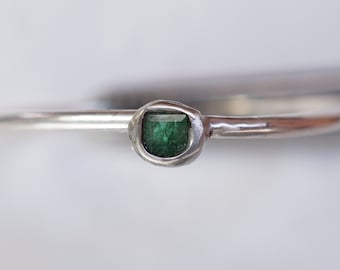 May include: A silver ring with a green gemstone set in a textured band.