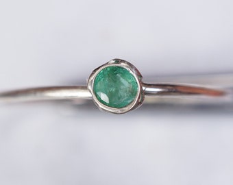 May include: A silver ring with a green emerald gemstone set in a bezel setting.