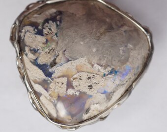 May include: A silver pendant with a large, irregular-shaped opal stone. The opal has a milky white base with flashes of blue, green, and purple.