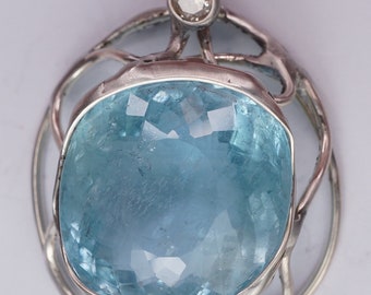 Può includere: Un ciondolo d'argento con una grande pietra di acquamarina blu chiaro incastonata in un delicato design traforato. Un diamante più piccolo e trasparente è incastonato nella parte superiore del ciondolo.