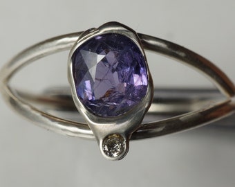 Puede incluir: Un anillo de plata con una piedra preciosa púrpura y un pequeño acento de diamante. El anillo tiene un diseño único y orgánico.