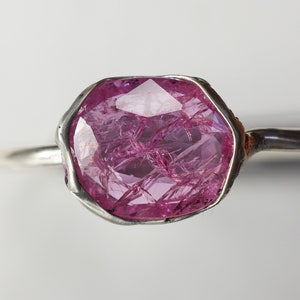 May include: A silver ring with a large, faceted, pink gemstone set in a bezel setting.