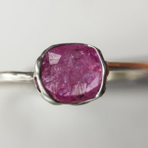 Op de afbeelding: Een zilveren ring met een roze edelsteen gezet in een getextureerde zetting. De edelsteen is ruw geslepen en heeft een natuurlijke, organische uitstraling.