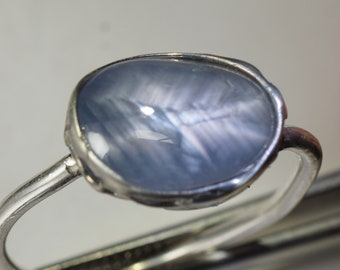 Puede incluir: Un anillo de plata con una piedra ovalada azul claro. La piedra tiene un efecto brillante e iridiscente.