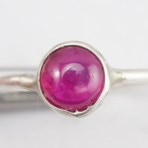 May include: A silver ring with a pink gemstone set in a bezel setting.