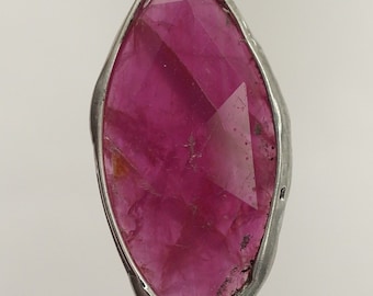 May include: A silver pendant featuring a large, faceted, pink ruby gemstone.