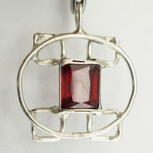 May include: A silver pendant with a geometric design featuring a red gemstone in the centre.