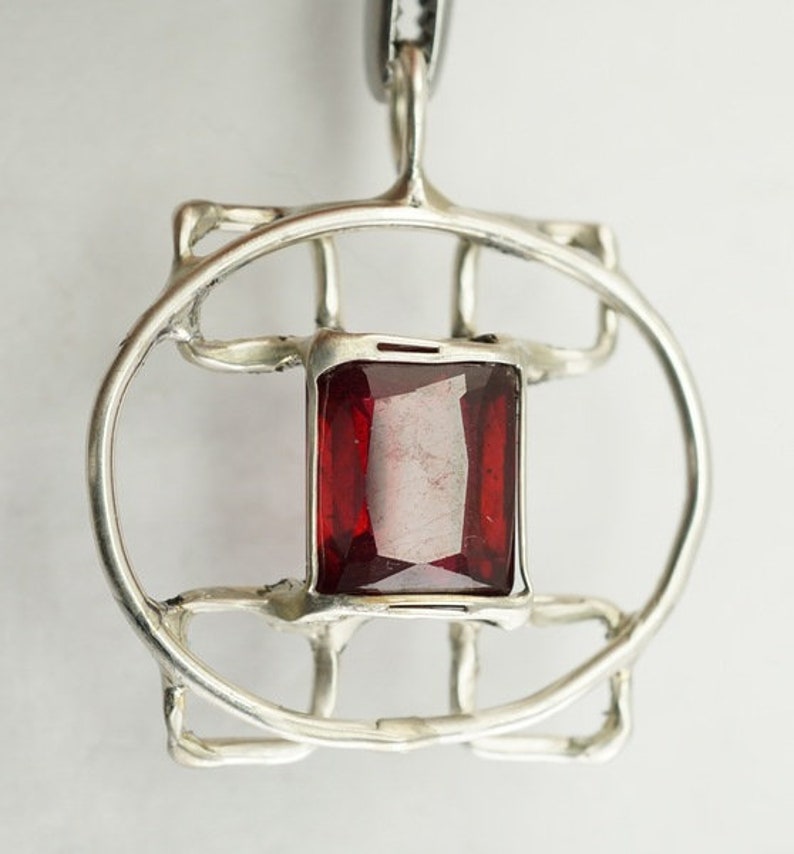 May include: A silver pendant with a geometric design featuring a red gemstone in the centre.