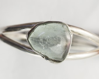 May include: A silver ring with a light green, faceted gemstone set in a bezel setting.