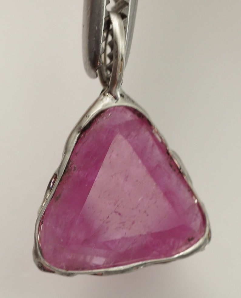 May include: A triangular pink gemstone pendant with a silver setting. The pendant is hanging from a silver chain.