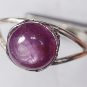 May include: A silver ring with a large, round, cabochon-cut, purple ruby gemstone.