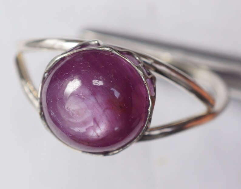 May include: A silver ring with a large, round, cabochon-cut, purple ruby gemstone.