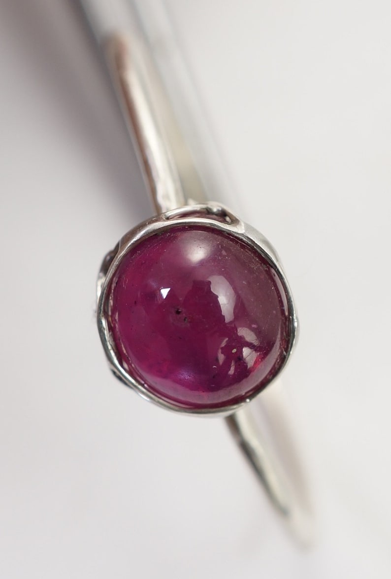 May include: A silver ring with a deep pink oval gemstone set in a textured bezel.
