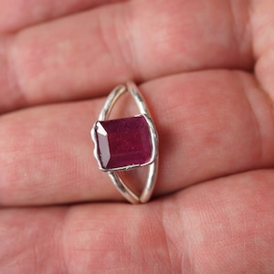 May include: A silver ring with a deep red gemstone set in a square shape.