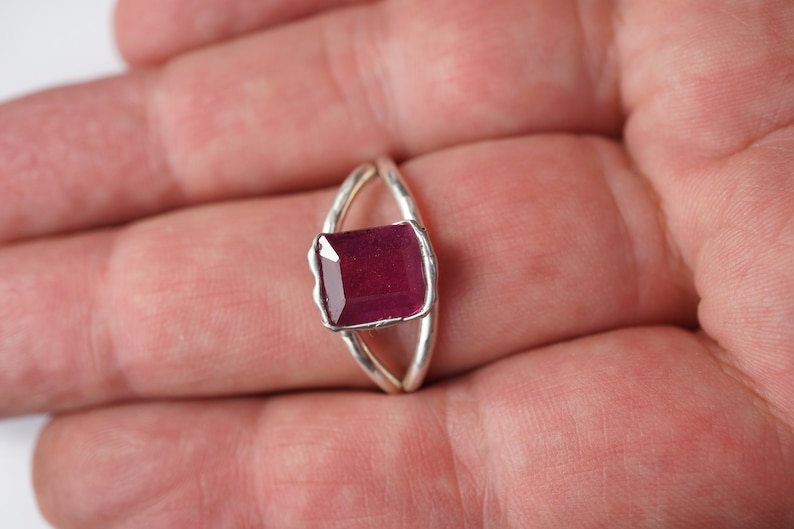 May include: A silver ring with a deep red gemstone set in a square shape.