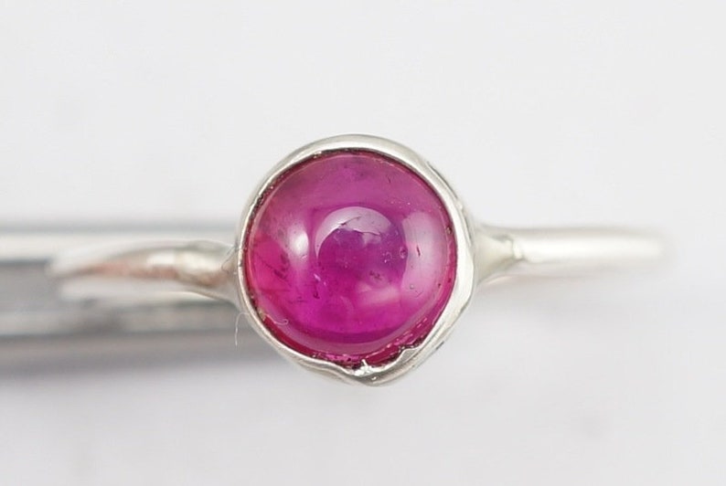May include: A silver ring with a pink gemstone set in a bezel setting.