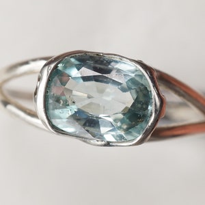 May include: A silver ring with a light blue oval gemstone set in a bezel setting.